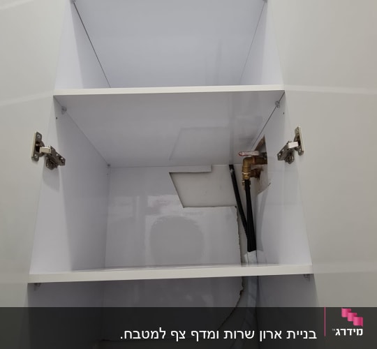 ארון לבן עם מדפים ודלתות פתוחות, צינור וגזע עץ.